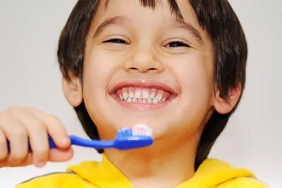 young boy smiling big while brushing his teeth